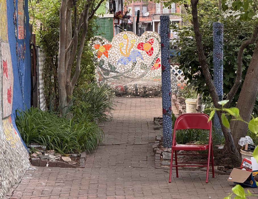 Horta comunitária com paredes de mosaico, árvores e arbustos.