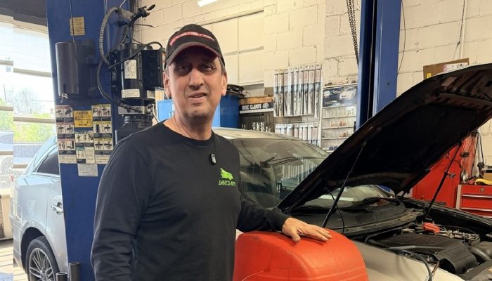 Richard Sanchez stands in front of a piece of equipment inside the garage next to a car with its hood open at Dave's Automotive in Tacony.